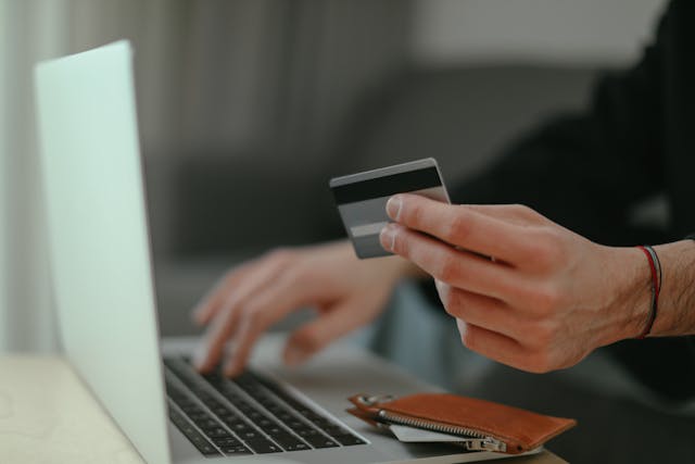 Person typing on a laptop with one hand and holding a bank card in the other hand